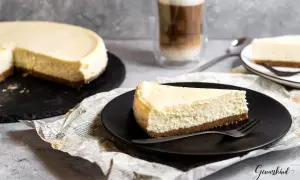 Ein Stück cremiger American Cheesecake, perfekt für das original american cheesecake rezept. Dazu ein Latte Macchiato.