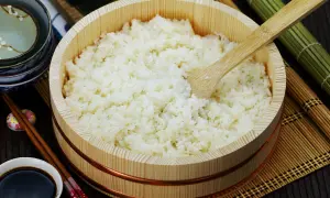 Perfekt zubereiteter sushi reis in einem hölzernen Behälter, bereit für die Zubereitung von Sushi. Daneben liegen Stäbchen und Sojasauce.