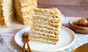 Ein Stück russischer Kuchen, geschichtet mit Honig und Sahne, auf einem Teller mit goldenem Besteck.