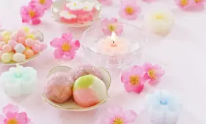Zarte japanische Desserts, bunte Süßigkeiten und blütenförmige Kerzen auf rosa Untergrund.