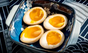 Vier halbe, perfekt gekochte ramen eier mit flüssigem Eigelb in einer blauen Schale mit Kirschblütenmuster.