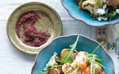 Gewürzschale mit rotem Pulver, vielleicht eine Sumach-Alternative, neben einem bunten Salat mit Blumenkohl und Ziegenkäse.