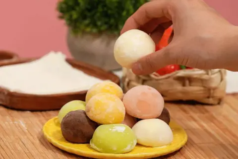 Bunte mochis eis in verschiedenen Geschmacksrichtungen auf einem gelben Teller. Eine Hand greift nach einem weißen mochi eis.