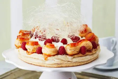 Ein prachtvoller Saint Honoré Kuchen mit Brandmasse-Profiteroles, frischen Himbeeren, Sahne und Karamellfäden.