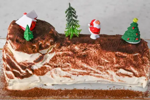 Eine festliche Bûche de Noël, dekoriert mit Weihnachtsmann, Bäumen und einem Haus.
