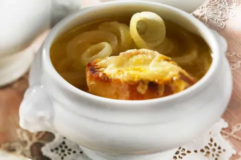 Herzhaftes Zwiebelsuppe Rezept Original: goldbraun überbackenes Brot mit geschmolzenem Käse auf Zwiebelringen in Brühe.