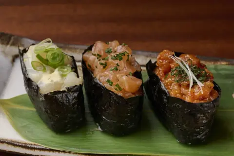 Drei leckere Sushi Gunkan mit Lachs, Garnelen und Fisch, garniert mit Frühlingszwiebeln und Kräutern.