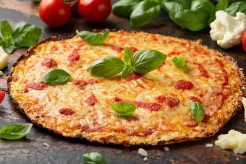 Eine köstliche blumenkohl pizza vegan, belegt mit Tomaten und Käse, garniert mit frischem Basilikum.