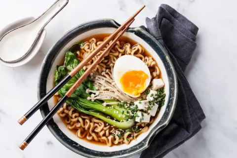 Schüssel mit japanischem Ramen, Nudeln, Ei, Gemüse und Tofuwürfeln, garniert mit Sesam und Schnittlauch.
