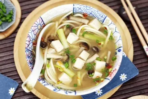 Herzhafte Miso Udon Suppe mit Tofu, Pilzen und Frühlingszwiebeln, serviert in einer dekorativen Schale.