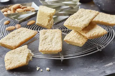 Goldbraune Financiers, frisch aus dem Ofen, warten auf das Financier Rezept. Mandeln liegen daneben.
