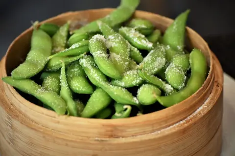Salzige Edamame-Schoten in einem Bambuskorb. Was ist Edamame? Junge Sojabohnen, eine gesunde und leckere Vorspeise.