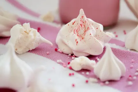 Zarte Baisers, frisch aus dem Ofen, sind nach dem Backen leicht klebrig. Kleine Zuckerperlen zieren die süßen Leckereien.
