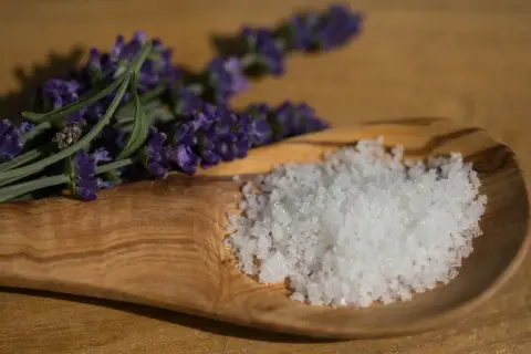 Fleur de Sel, feine Meersalzkristalle, auf einem Olivenholz-Löffel neben Lavendel. Was ist Fleur de Sel? Ein Hauch von Luxus für Ihre Küche.