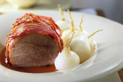 Boeuf à la mode: Ein saftiges Stück Rindfleisch, umwickelt mit knusprigem Speck, serviert mit kleinen, glasierten Zwiebeln in einer köstlichen Sauce.