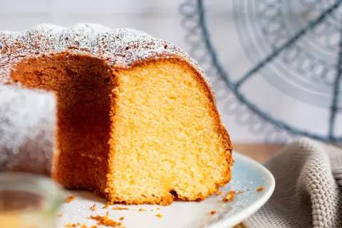 Saftiger Kuchen mit 12 Eiern, bestäubt mit Puderzucker, auf einem Teller mit einem Stück herausgeschnitten.
