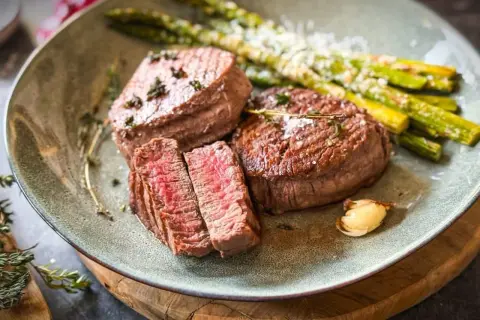 Zartes Filet de Boeuf, perfekt medium-rare gebraten, serviert mit grünem Spargel und einer Knoblauchzehe. Ein Festmahl!