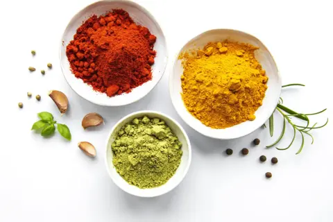 Schalen mit roten, gelben und grünen Gewürzen, Knoblauch und Kräutern – die Zutaten, woher kommt Curry.