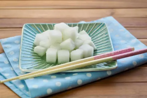 Würfel von daikon rettich auf einem grünen Teller, daneben Stäbchen auf einem blauen Tupftuch.