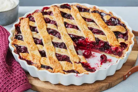 Ein frisch gebackener Kirschkuchen mit Gittermuster, perfekt für ein Kirschkuchen Rezept. Daneben eine Schüssel Schlagsahne.