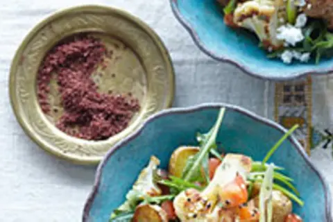 Gewürzschale mit rotem Pulver, vielleicht eine Sumach-Alternative, neben einem bunten Salat mit Blumenkohl und Ziegenkäse.