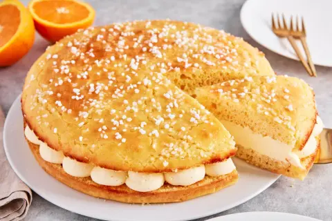 Eine köstliche Tarte Tropezienne, bestreut mit Zuckerperlen, gefüllt mit cremiger Vanillecreme. Daneben liegen Orangen.