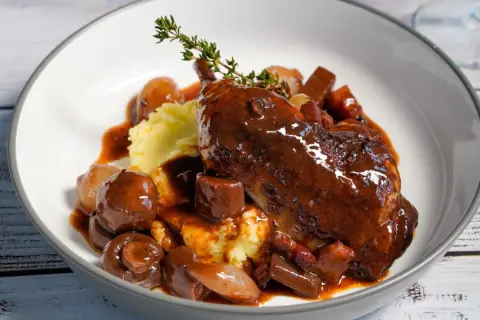 Ein authentisches Coq au Vin Rezept Original: zartes Hähnchen in Rotwein, serviert mit Kartoffelpüree, Speck und glasierten Zwiebeln.