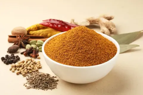 Eine Schüssel mit dem würzigen Pulver, das ist garam masala, umgeben von ganzen Gewürzen wie Zimt, Sternanis, Kardamom, Nelken, Pfeffer, Koriander, Kreuzkümmel, Ingwer und Chili.