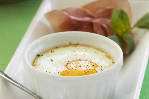 Ein köstliches oeuf cocotte mit einem perfekt gebratenen Ei, bestreut mit Pfeffer, serviert mit Schinken und Basilikum.
