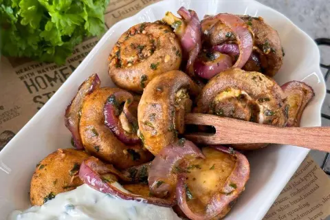 Gefüllte champignons aus dem airfryer mit roten Zwiebeln und Kräutern, serviert mit Dip.