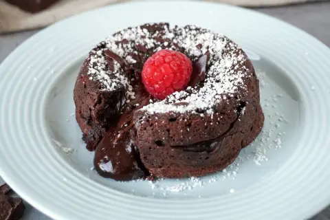 Schokokuchen mit weichem Kern, bestäubt mit Puderzucker und garniert mit einer Himbeere. Der flüssige Kern läuft verführerisch heraus.