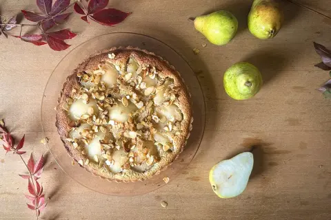 Eine köstliche Tarte Bourdaloue mit Birnen und Mandelsplittern, umgeben von frischen Birnen und herbstlichen Blättern auf Holzhintergrund.