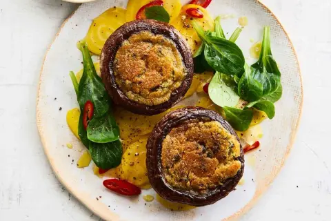 Zwei gefüllte Portobello Pilze auf gelben Ringen, garniert mit frischem Grün und Chilischeiben.