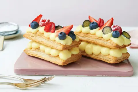 Zwei Mille-feuille-Törtchen mit Vanillecreme und frischen Beeren, bereit zum Genießen.