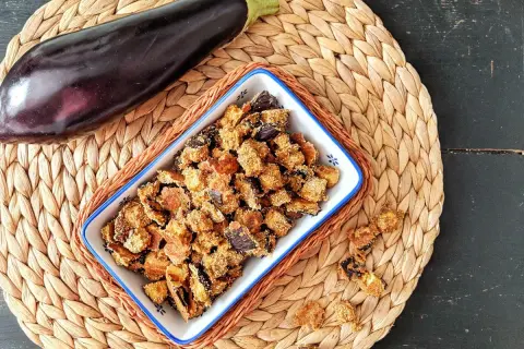 Knusprige, frittierte Aubergine in einer Schale, daneben eine ganze Aubergine. Ein leckerer Snack!
