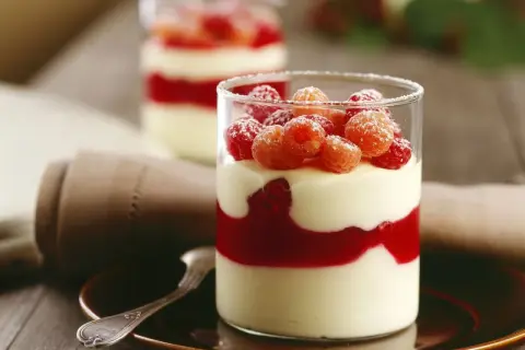 Zwei Gläser mit Schichten von Mousse au Chocolat Blanc, Himbeersauce und frischen Himbeeren, bestäubt mit Puderzucker.