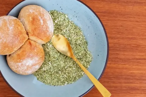 Drei Brötchen liegen auf einem Teller neben einer grünen Mischung, die zeigt, was ist schabzigerklee. Eine goldene Löffel liegt darin.