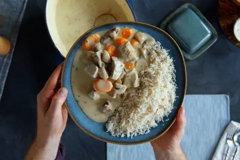 Ein Teller mit cremigem Blanquette de veau, Pilzen und Karotten, serviert mit Reis.