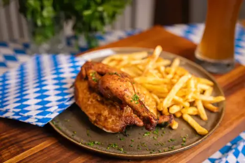 Ein knuspriger poulet roti mit Pommes Frites, garniert mit Kräutern, auf einem Teller mit blau-weiß karierter Serviette und einem Glas Bier.