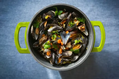 Ein Topf voller dampfender Moules Marinière, garniert mit frischer Petersilie und Karottenstücken, bereit zum Genuss.
