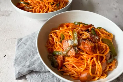Zwei Schüsseln mit leckerem Spaghetti Napolitan, garniert mit Paprika und Wurst.