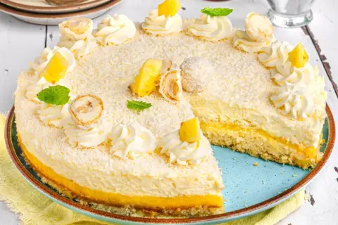 Ein köstlicher Ananas Kokos Kuchen, verziert mit Kokosraspeln, Sahnetuffs, Ananasstücken und Minze.