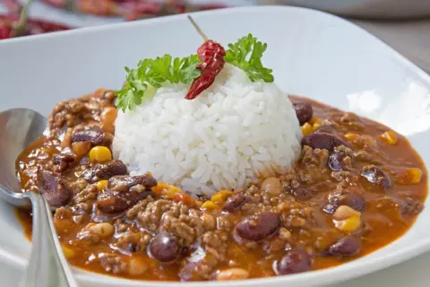 Herzhaftes Chili con Carne mit Reis, garniert mit Petersilie und einer getrockneten Chili.