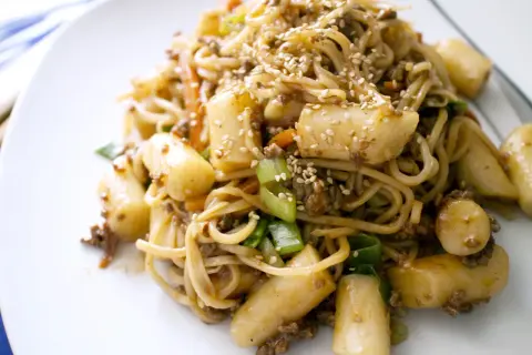 Yaki soba mit Hackfleisch, Möhren, Frühlingszwiebeln und Tteok (Reiskuchen), bestreut mit Sesam.