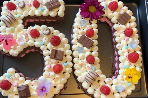 Ein aufwendig dekorierter Number Cake in Form der Zahl 50, verziert mit Sahnetuffs, Himbeeren, Schokolade und Blumen.