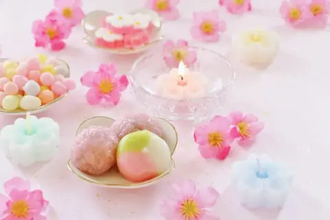 Zarte japanische Desserts, bunte Süßigkeiten und blütenförmige Kerzen auf rosa Untergrund.