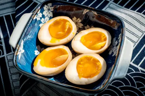 Vier halbe, perfekt gekochte ramen eier mit flüssigem Eigelb in einer blauen Schale mit Kirschblütenmuster.