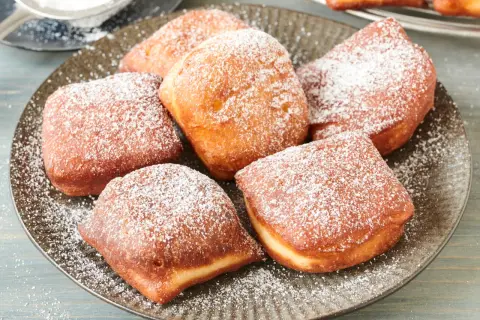 Leckere, goldbraune Beignets, bestäubt mit Puderzucker. Dieses Beignets Rezept ist ein Genuss!