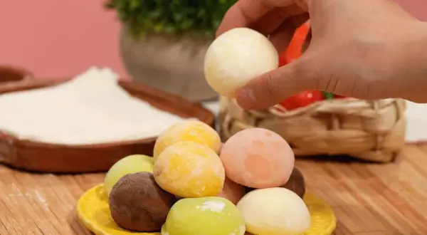 Bunte mochis eis in verschiedenen Geschmacksrichtungen auf einem gelben Teller. Eine Hand greift nach einem weißen mochi eis.