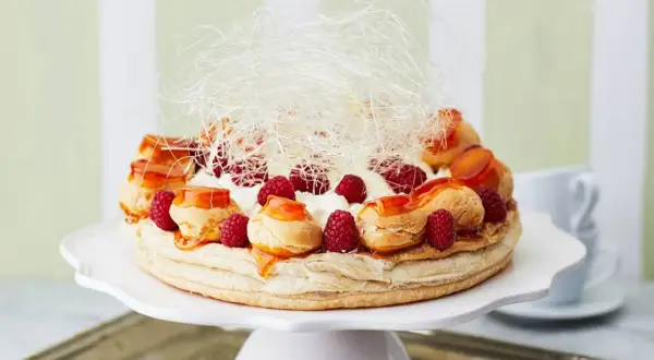 Ein prachtvoller Saint Honoré Kuchen mit Brandmasse-Profiteroles, frischen Himbeeren, Sahne und Karamellfäden.